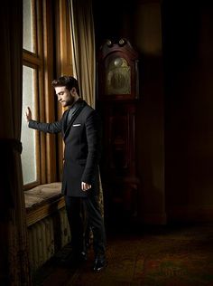 a man in a tuxedo leaning against a window with his hand on the window sill