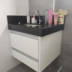 a bathroom sink sitting under a mirror next to a white cabinet with black counter top