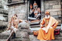 two men with painted faces sit on steps in front of a building, while another man sits next to them