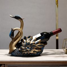 a wine bottle holder that is shaped like a swan sitting on a table next to a glass of wine