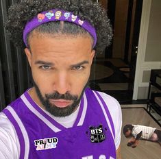 a man with an afro wearing a purple basketball jersey and headband in front of him