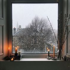 a window sill filled with candles next to a window covered in snow and trees