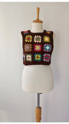 a white mannequin wearing a brown sweater with colorful crocheted flowers on it