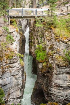 a bridge over a river that is surrounded by tall rocks and greenery on both sides