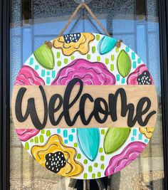 a welcome sign hanging on the front door of a building with flowers painted on it