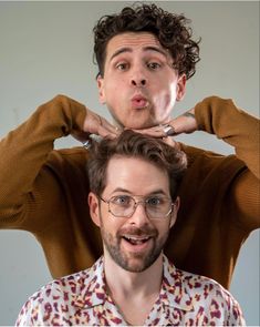 a man with glasses making a funny face while standing in front of another man's head