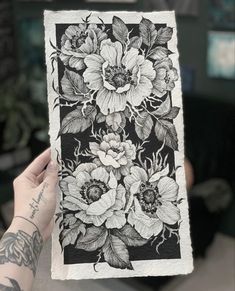 a person holding up a black and white drawing with flowers on it's side