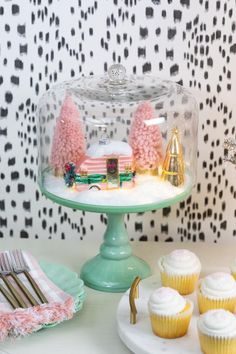 cupcakes and cakes are under a glass clochet on a table with black and white wallpaper