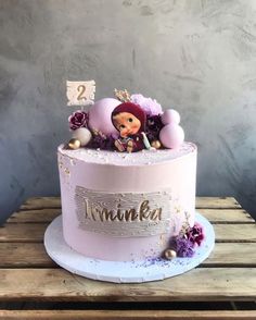 a pink birthday cake decorated with an image of a doll and flowers on top, sitting on a wooden table