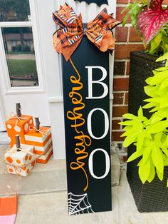 a sign that says booo on it next to flowers and pumpkins in front of a house