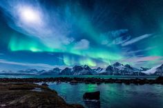 the aurora bore is shining brightly in the night sky over water and mountains with snow on them