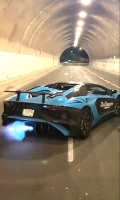 a blue sports car driving through a tunnel with lights on it's side and the door open