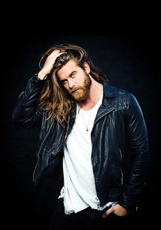 a man with long hair wearing a black leather jacket and white t - shirt is posing for the camera