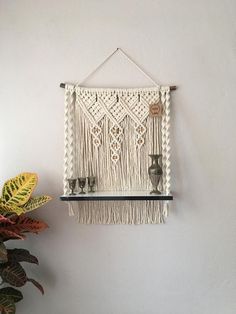 a macrame wall hanging with two candles on it and a potted plant next to it