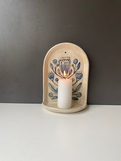 a lit candle is sitting in a small holder on a table with a gray wall behind it