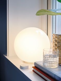 a white lamp sitting on top of a window sill next to a glass vase