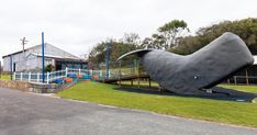 a large metal whale sculpture sitting on top of a lush green field next to a building