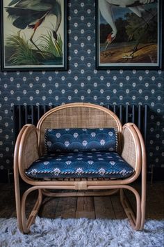 a wicker chair with blue cushions in front of two framed pictures on the wall