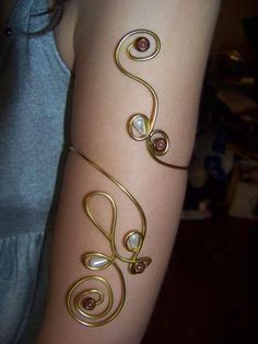 a woman's arm with gold wire and pearls on it