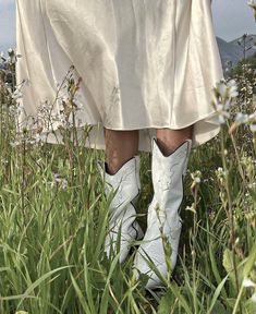 a woman standing in tall grass wearing white cowboy boots