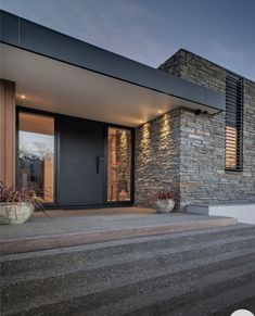 a modern house with stone walls and steps leading up to the front door at dusk