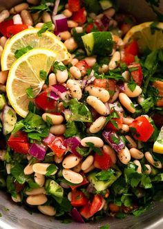 a salad with beans, tomatoes, cucumbers and lemon wedges is shown in a bowl