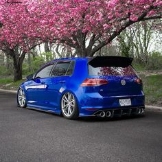 a blue car parked on the side of a road next to trees with pink flowers