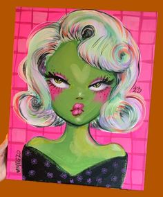 a painting of a woman's face with green hair and bright pink eyes is being held up