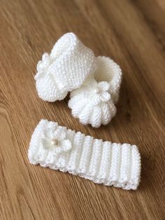 two white knitted baby booties on a wooden floor next to a pair of shoes