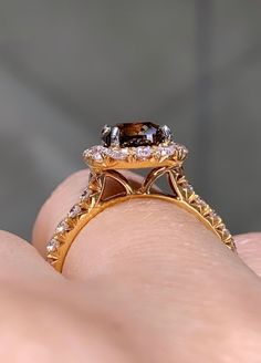 a close up of a person's hand holding an engagement ring with a brown diamond