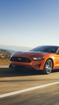 an orange ford mustang driving down the road