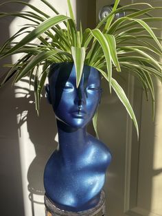 a blue mannequin head with a plant in it