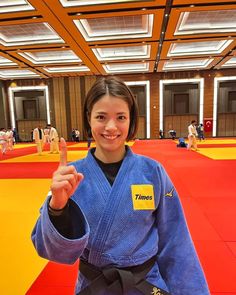 a woman in a blue kimono standing on a red and yellow mat with her finger up