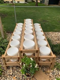 a wooden pallet filled with lots of white bowls on top of gravel next to a fence
