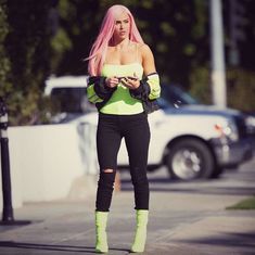 a woman with pink hair and green boots is looking at her cell phone while standing on the street
