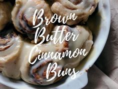 a white bowl filled with cinnamon buns on top of a cloth covered tablecloth