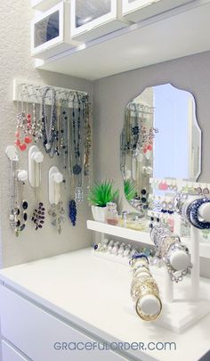 a white dresser topped with lots of necklaces next to a wall mounted jewelry rack