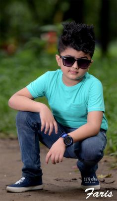 a young boy wearing sunglasses crouches on the ground