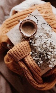 an open book, coffee cup and flowers on a bed with a scarf around it