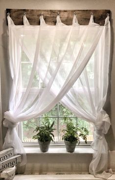 a window with white curtains and potted plants