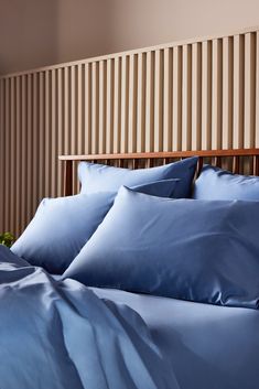a bed with blue sheets and pillows on top of the headboard in front of a striped wall