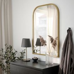 a black dresser with a mirror, lamp and plants on it in front of a window