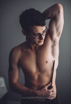 a shirtless young man holding a baseball bat in his right hand and wearing glasses