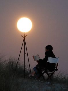 a person sitting in a chair next to a light on top of a hill at night