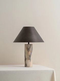 a table lamp sitting on top of a white tablecloth covered table with a black shade