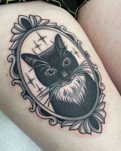 a black and white photo of a cat in a frame tattoo on the thigh with an ornate border around it