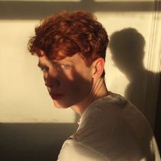 a man with red hair and blue eyes standing in front of a window looking at the camera