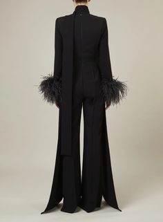 the back view of a woman wearing a black suit with feathers on it