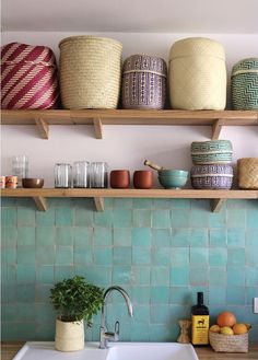 a kitchen sink sitting under two wooden shelves filled with bowls and baskets on top of it