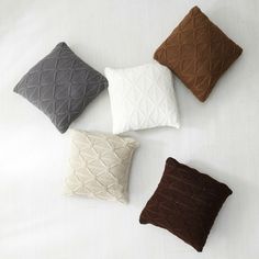 four different colored pillows sitting on top of a white bed sheet, one is brown and the other is grey